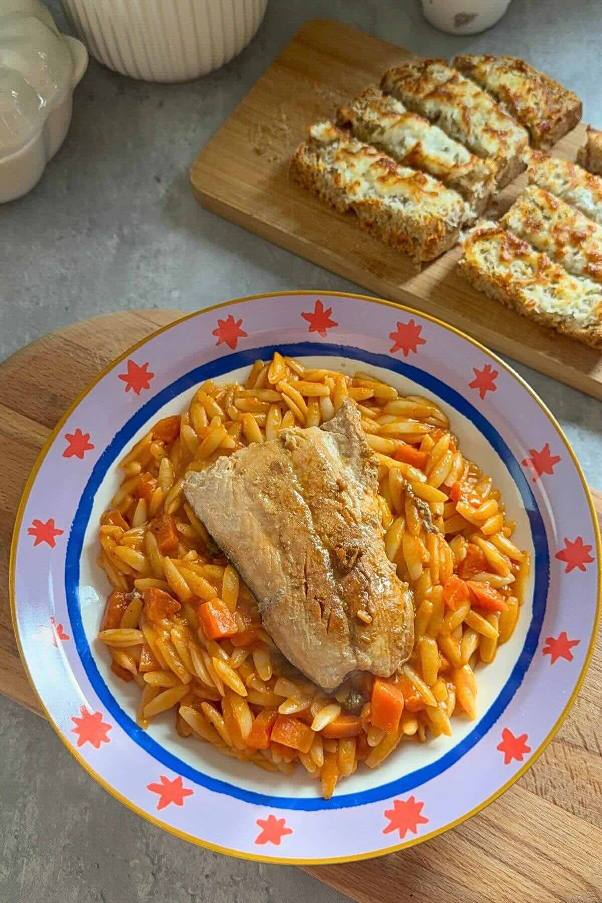 Creamy tomato orzo with baked salmon and fresh herbs in a bowl.