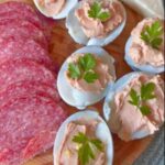 Deviled eggs, salami, cheese, tomatoes, olives, and egg spread on bread arranged on a plate.