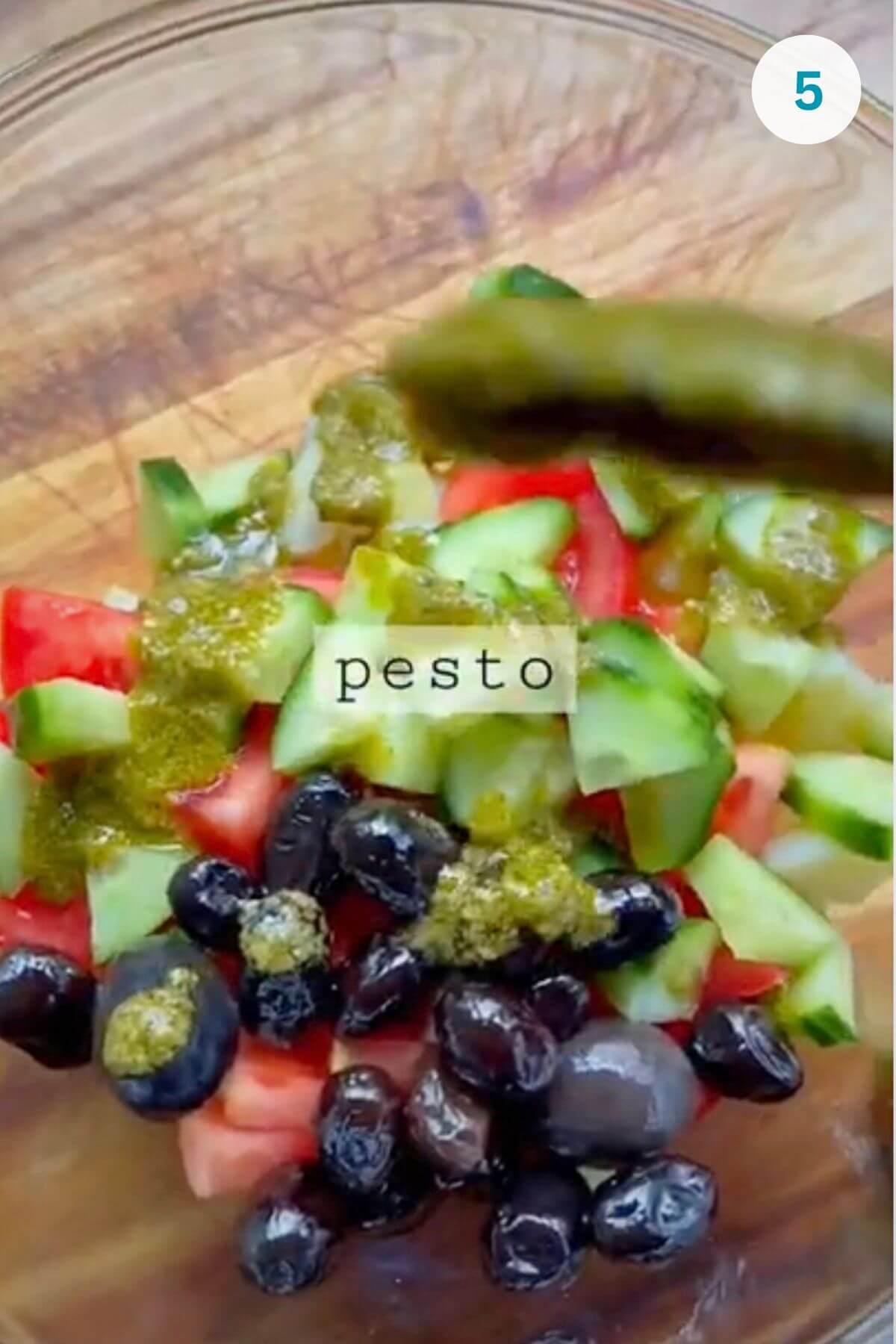 Spooning rich pesto dressing over the salad ingredients.