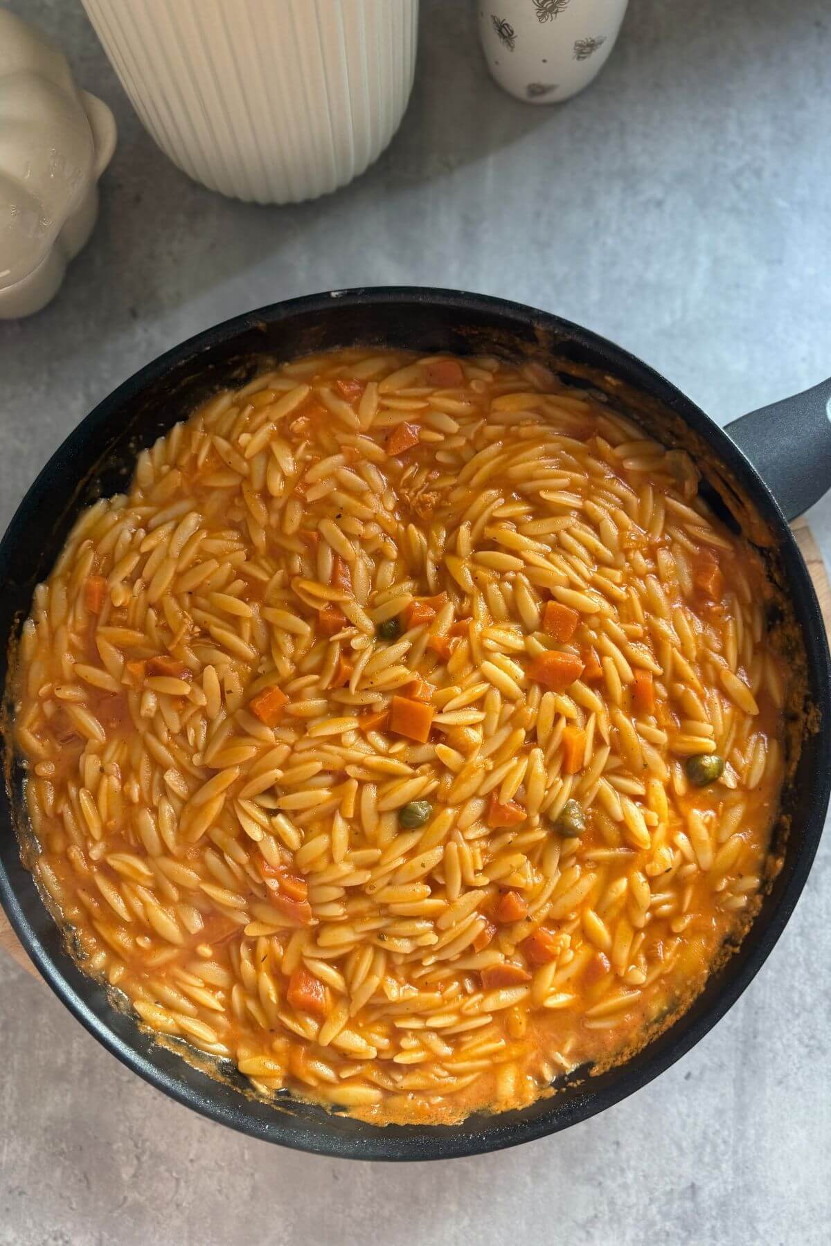 Creamy tomato orzo with capers ad carrot in a pan.