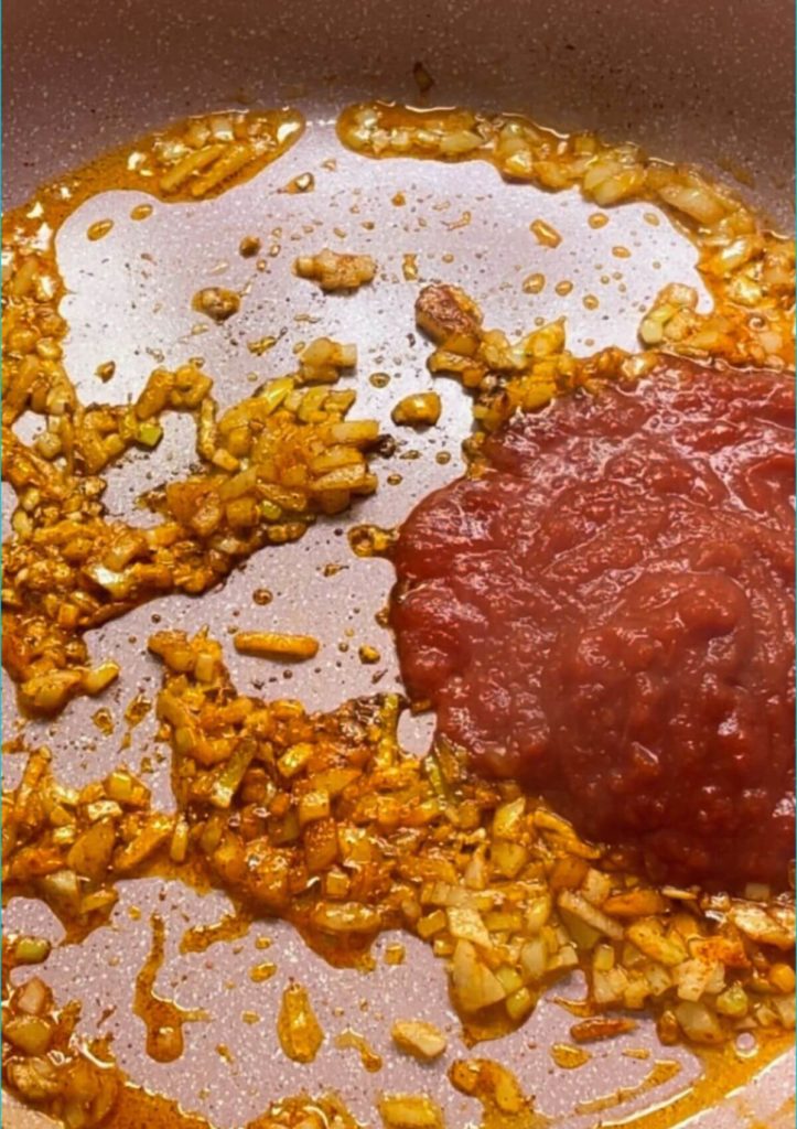 A pan with chopped onion, seasoned with salt, smoked paprika, and tomato sauce in one corner.