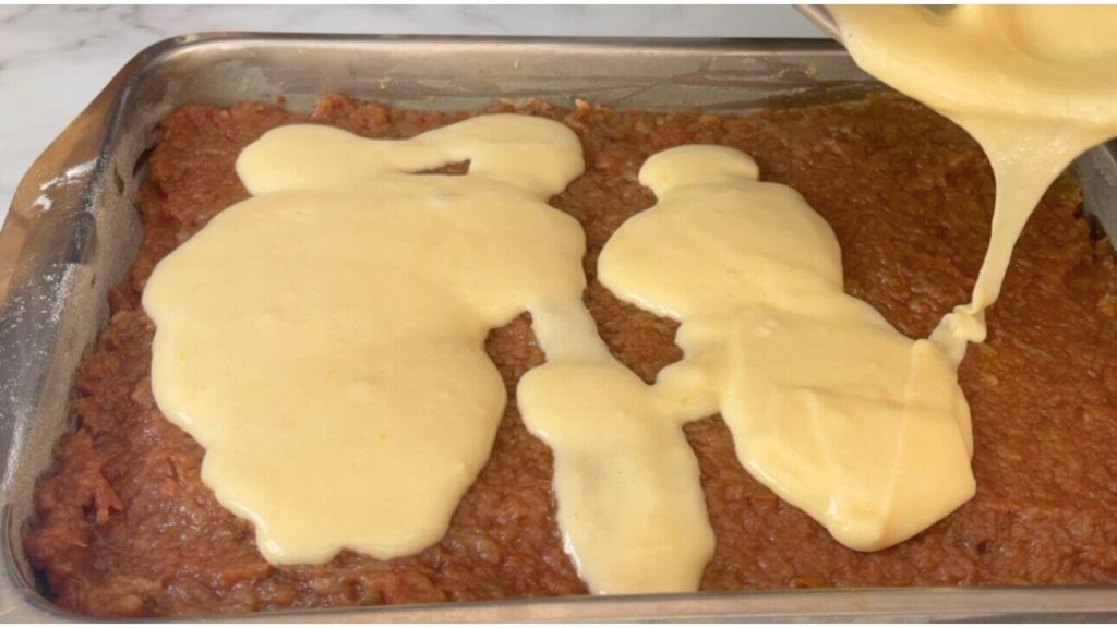 Adding the remaining uncooked batter over the apple filling in a rectangular pan, preparing it to be placed in the oven for making a delectable apple cake.