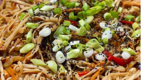 Chicken noodles in a pan, topped with fresh green onions and sesame seeds