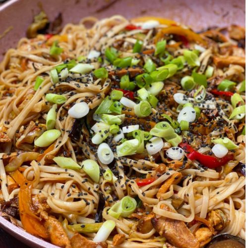 Chicken noodles in a pan, topped with fresh green onions and sesame seeds