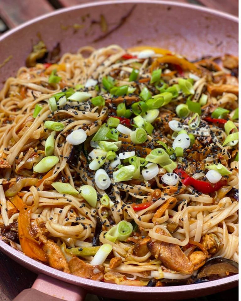 Chicken noodles in a pan, topped with fresh green onions and sesame seeds