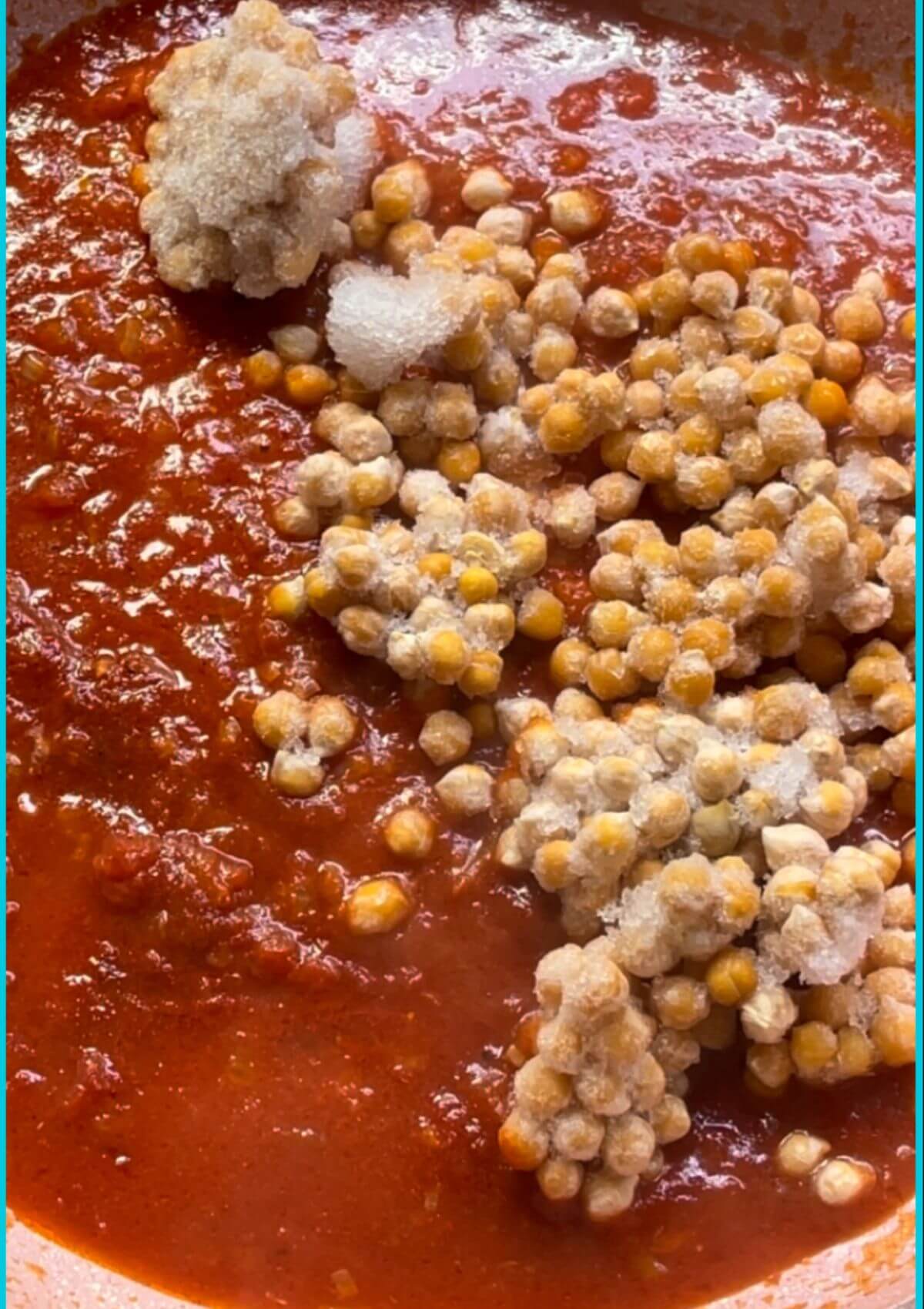 Chickpeas being added to a thickened tomato base in a pan, creating a flavorful and hearty dish. 