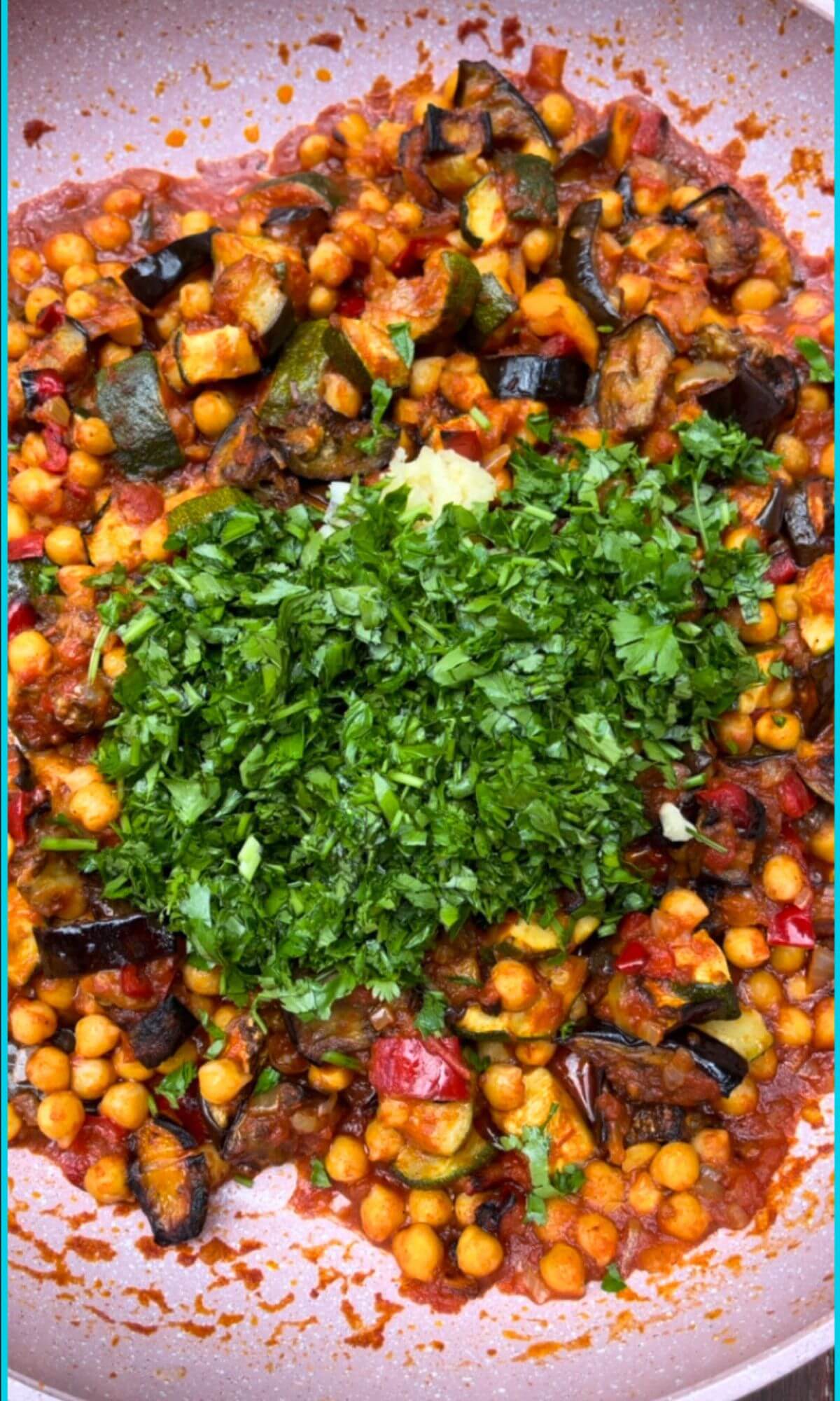 Delicious chickpea ratatouille in a pan, garnished with freshly chopped coriander and parsley, and two grated garlic cloves.