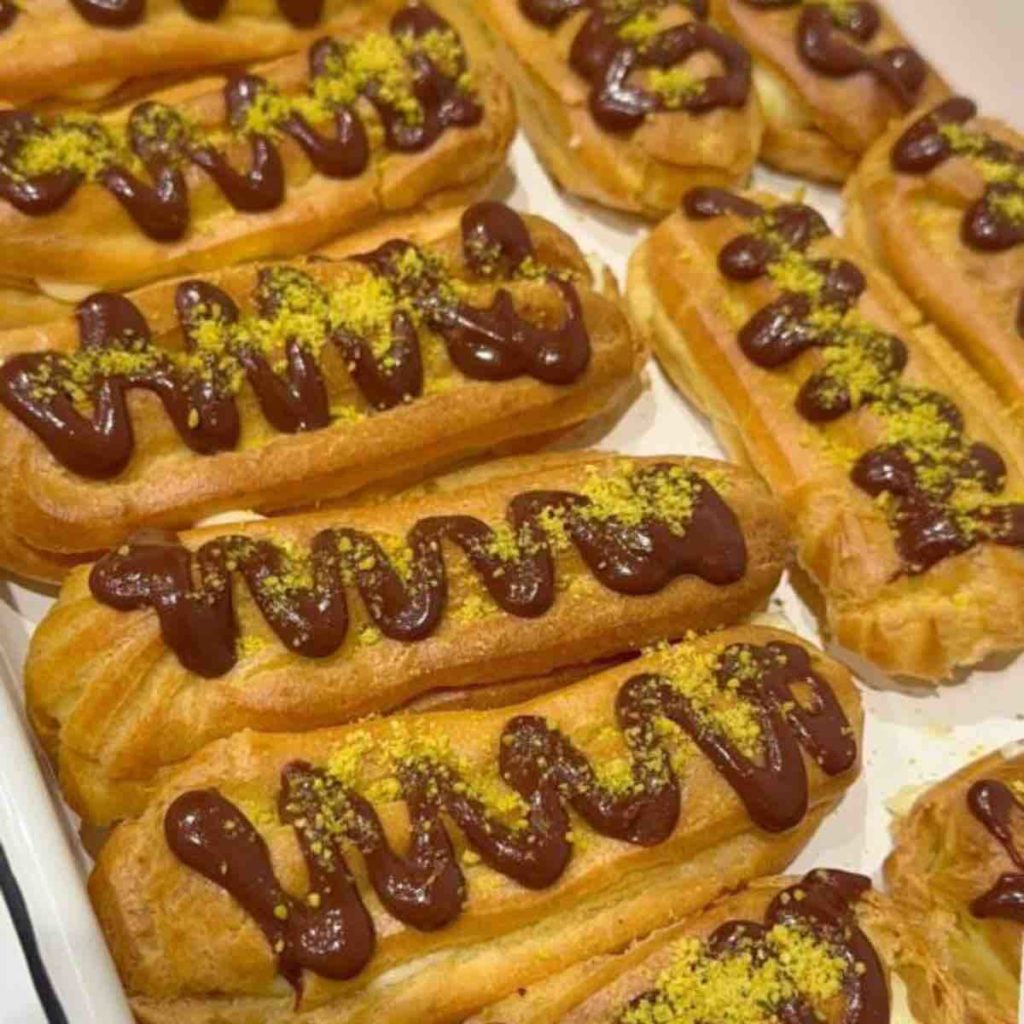 Eclairs on a tray topped with chocolate glaze and ground pistachio