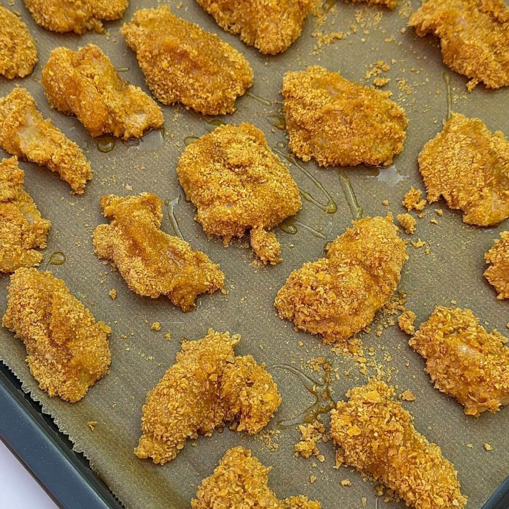 Raw chicken breast pieces seasoned and coated with breadcrumbs arranged on a baking tray.
