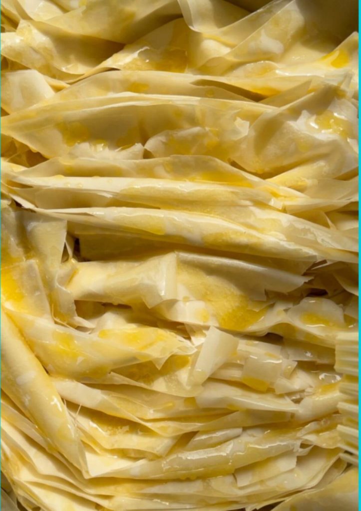 Phyllo sheets arranged in a baking pan with a delightful crinkle pattern, drizzled with melted butter.