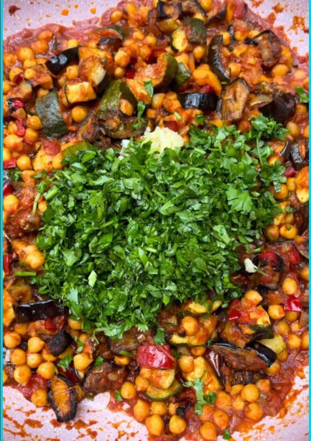 Chickpea ratatouille in pan with roasted veggies, fresh herbs, and grated garlic garnish. 