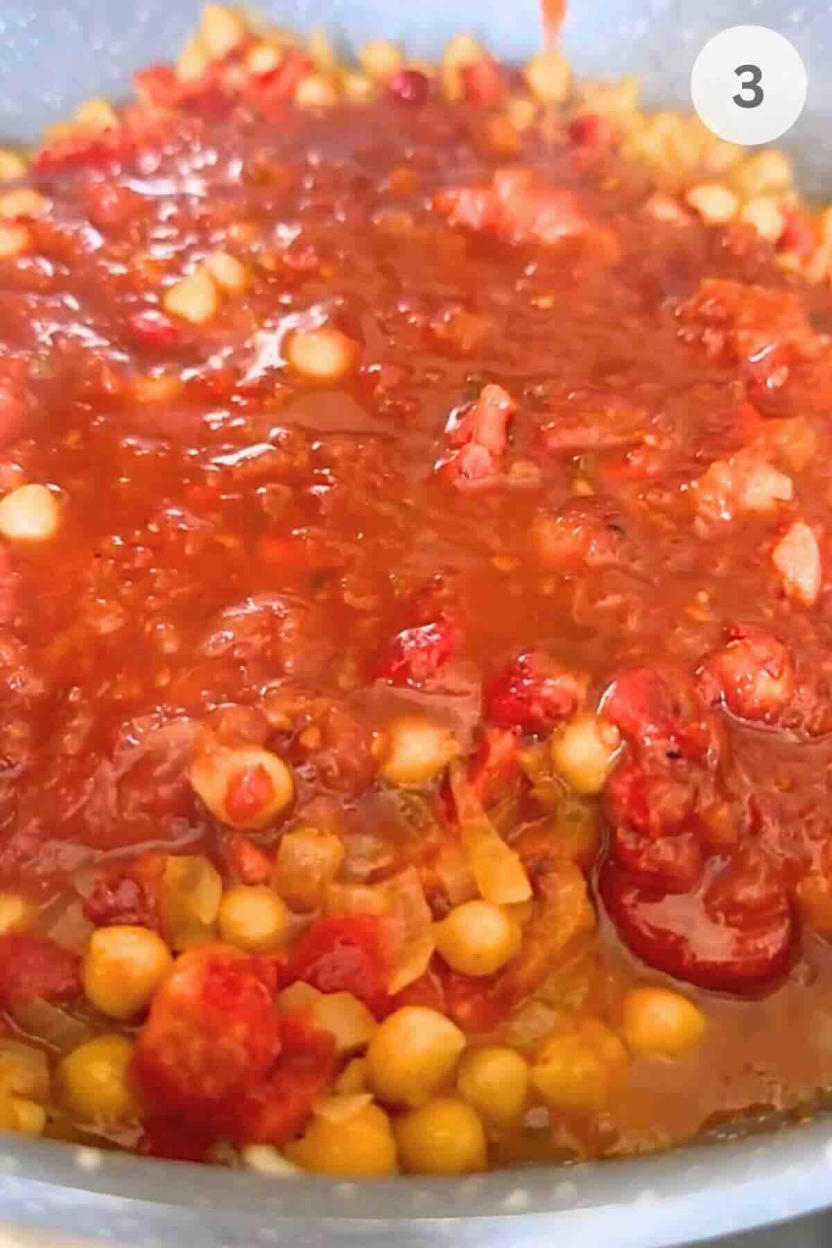 Tomato passata being poured into the skillet with peppers, onion, and chickpeas.