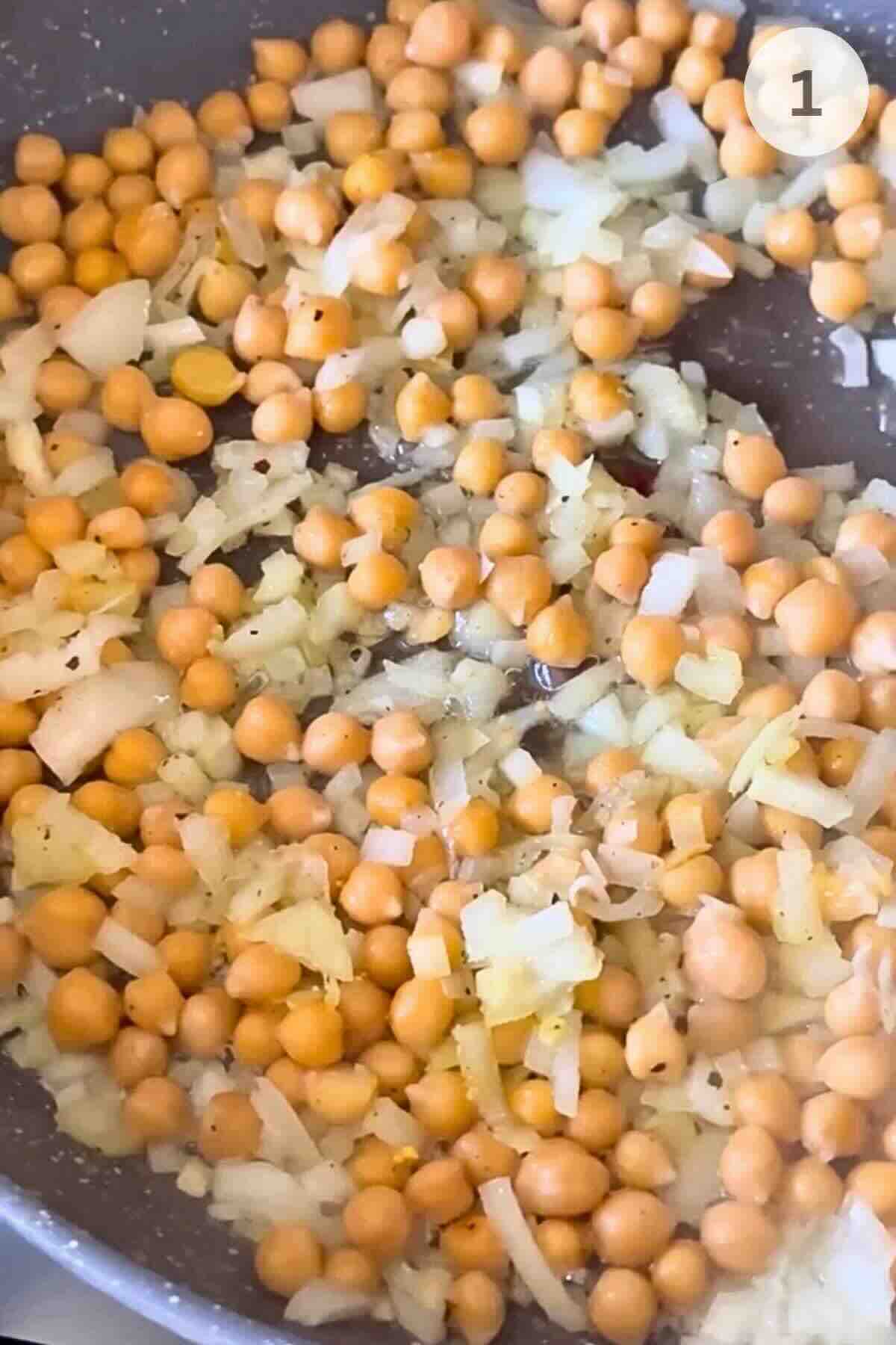 Chopped onion and chickpeas cooking in olive oil in a wide skillet.