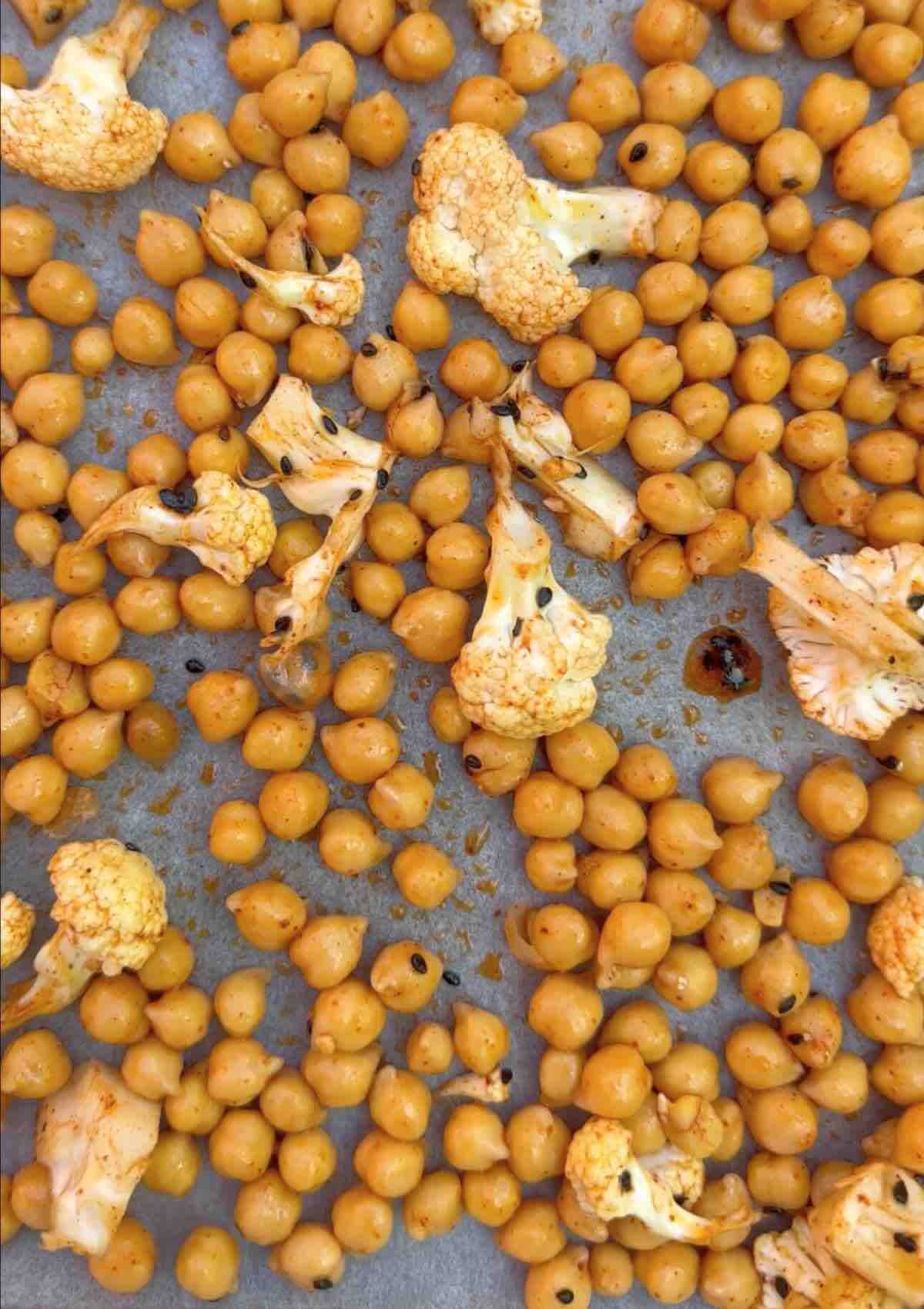Chickpeas and cauliflower florets covered in spices, spread out on a baking pan, ready to be baked.