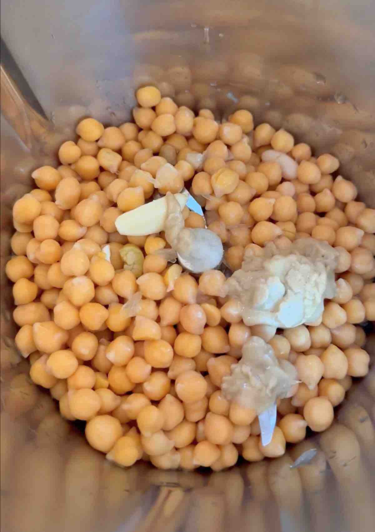 Chickpeas, tahini, lemon juice, aquafaba, salt, garlic, and olive oil in a mixing bowl, ready to be blended.