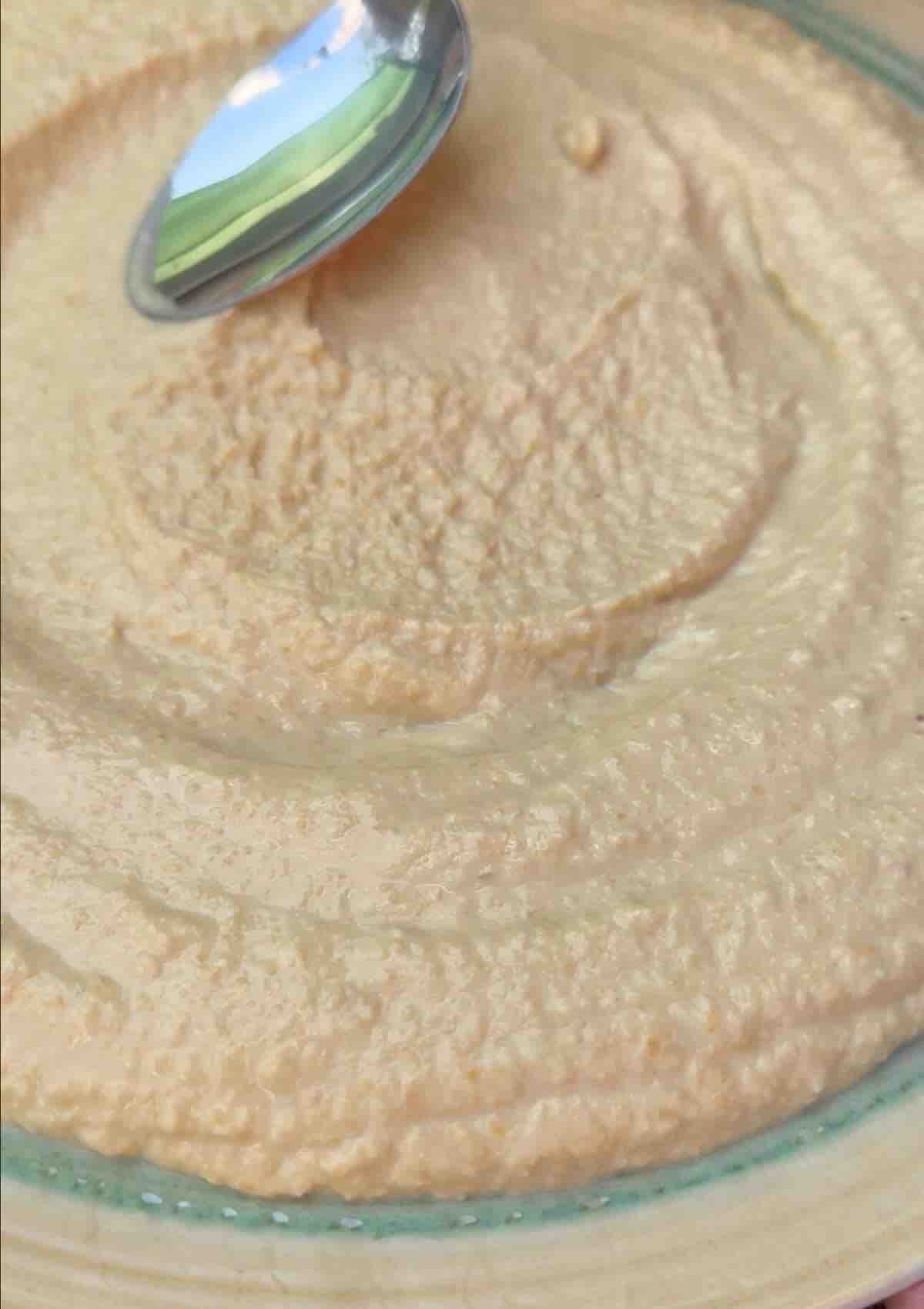 Creamy hummus spread out on a plate with a metal spoon.