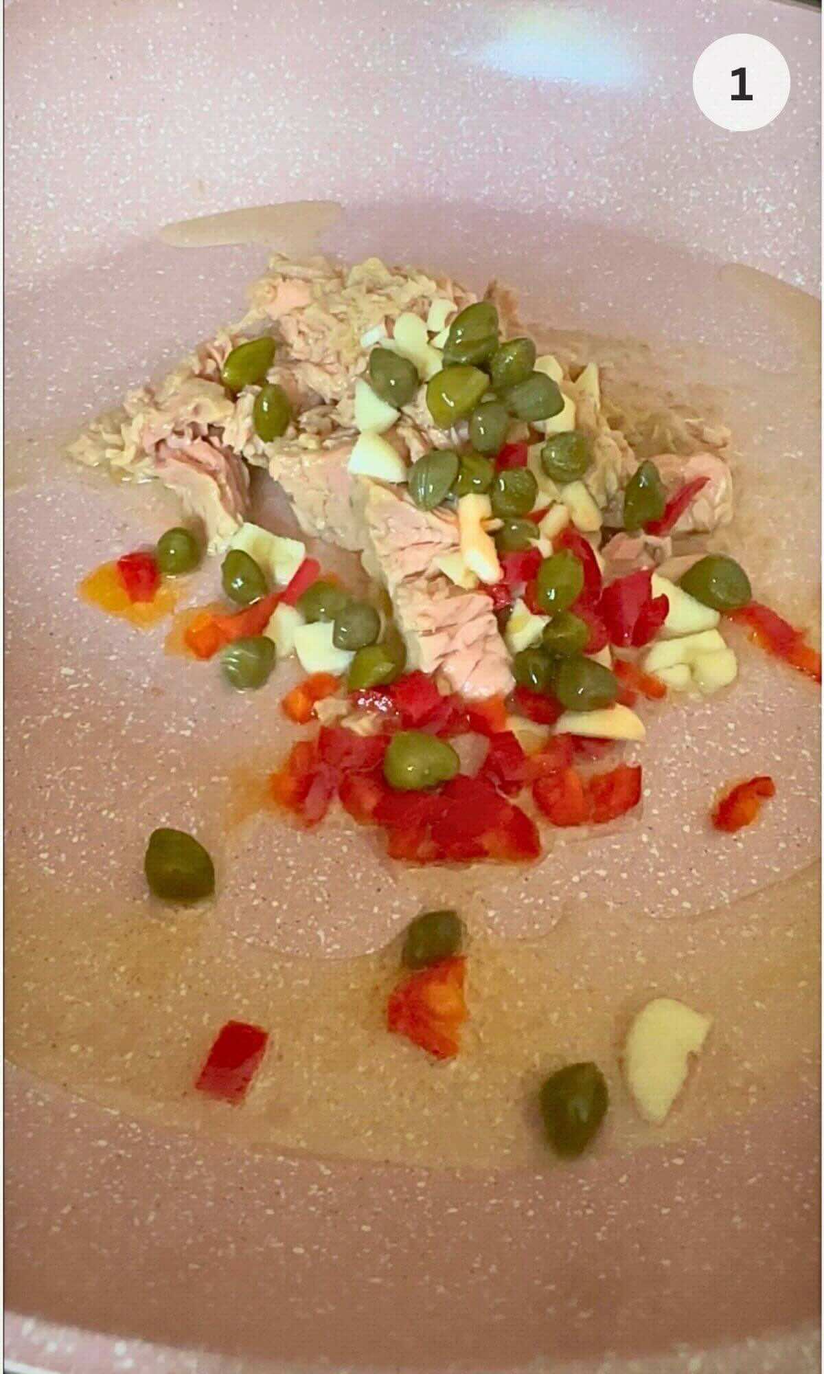 Pan with tuna chunks simmering in olive oil, garlic, chilli, and capers.