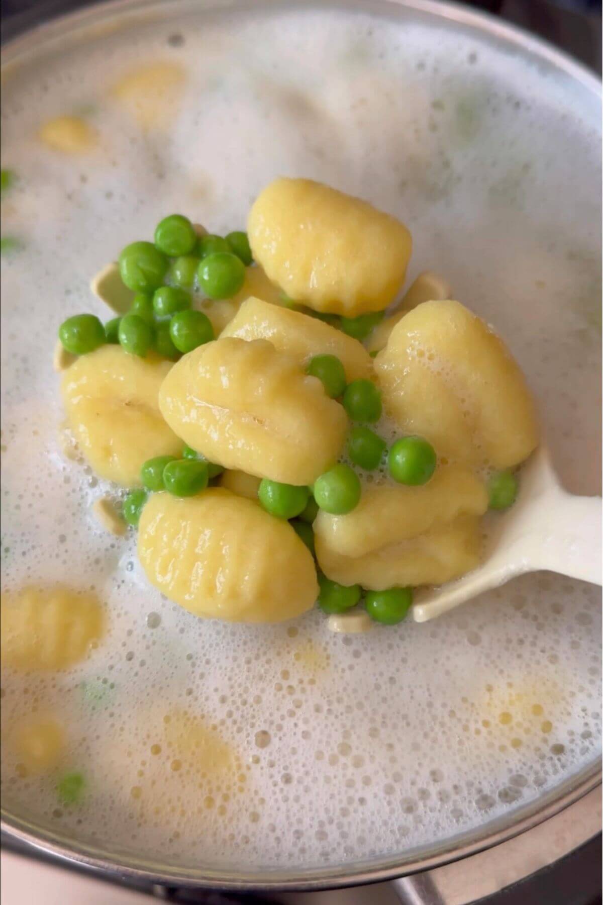 Gnocchi and peas lifted from the pot with a pasta spoon, steaming hot.