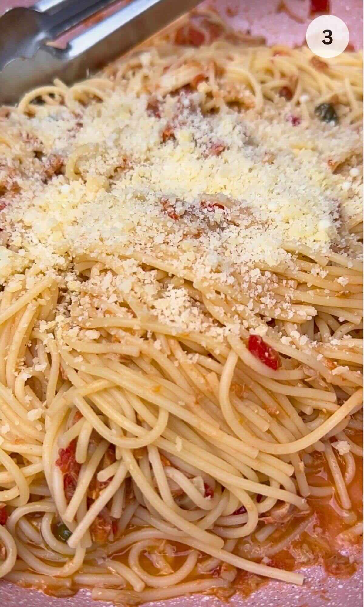 Pan with tuna in olive oil, garlic, chili, and capers in tomato sauce, with cooked spaghetti being added.