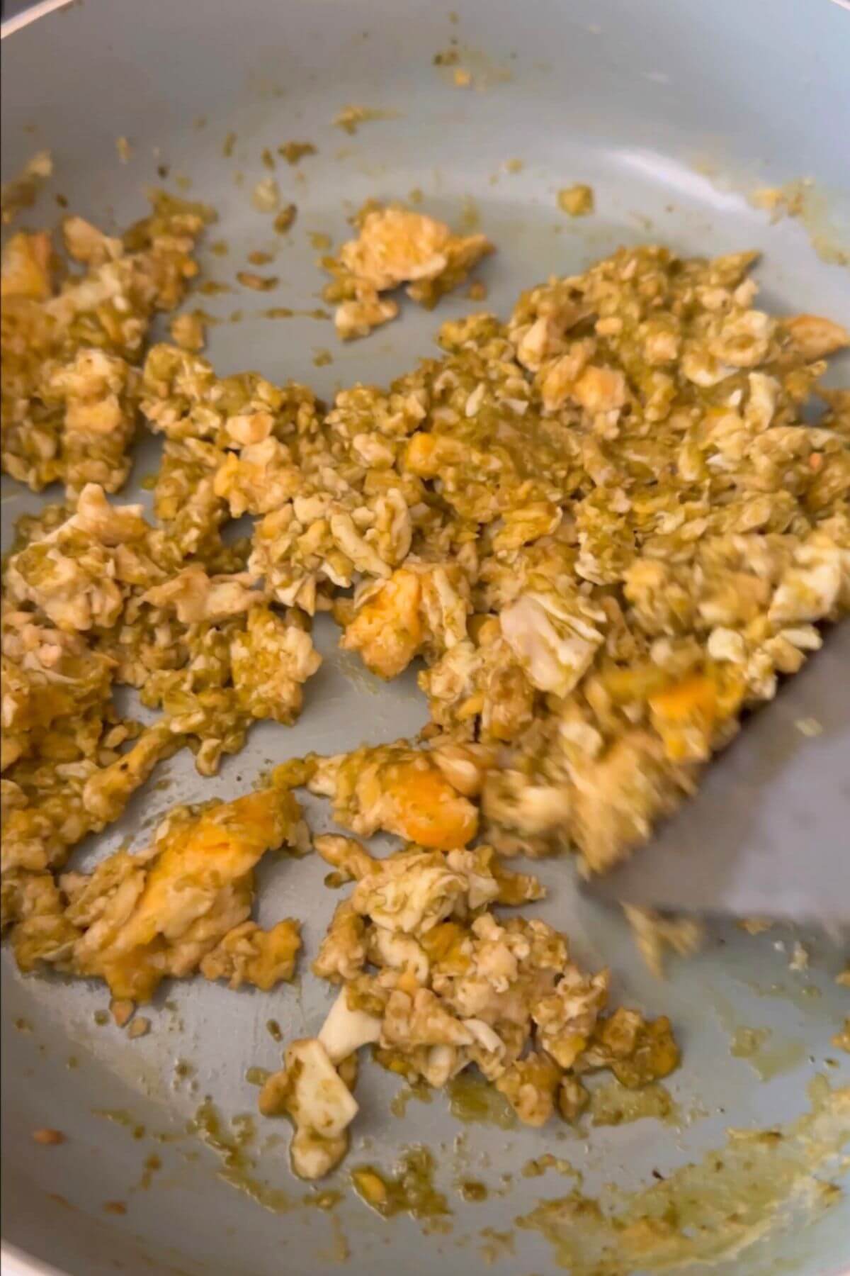 Crumbled omelette and pesto sauce mixed together in a pan.