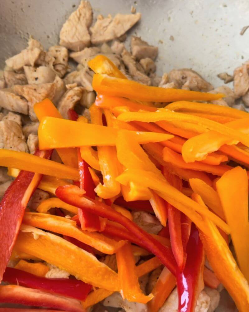 Chicken breast slices cooked in a pan with colorful peppers cut lengthwise.