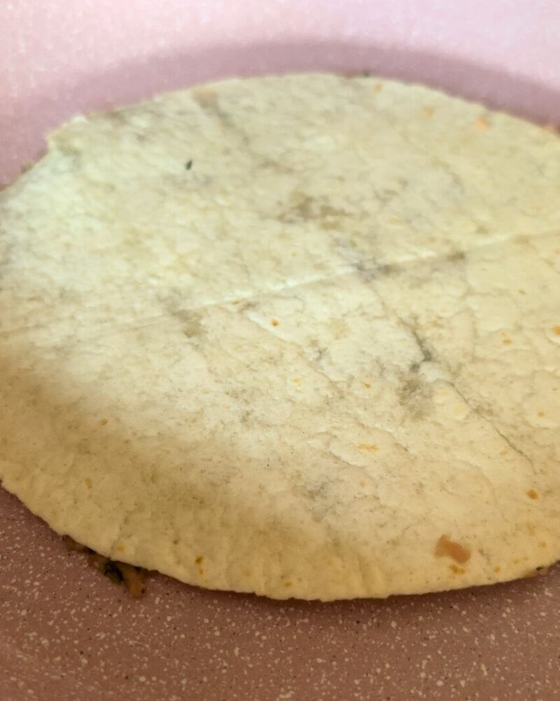 Kefta smashed on a tortilla placed upside down in a pan for frying, preparing Smashed Kefta Tacos