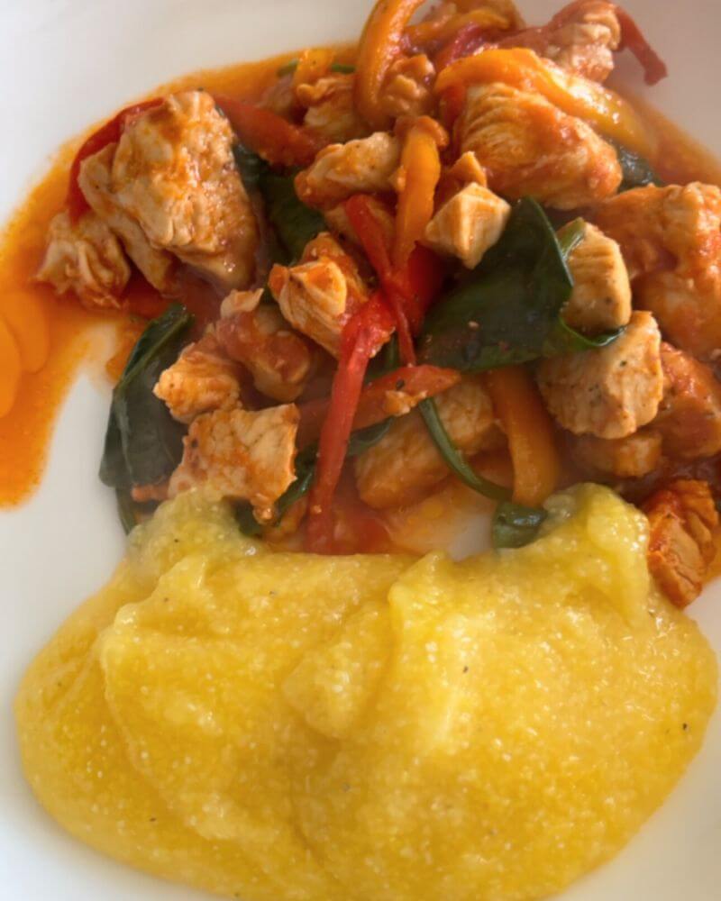 Chicken with spinach and peppers in tomato sauce, served with polenta.