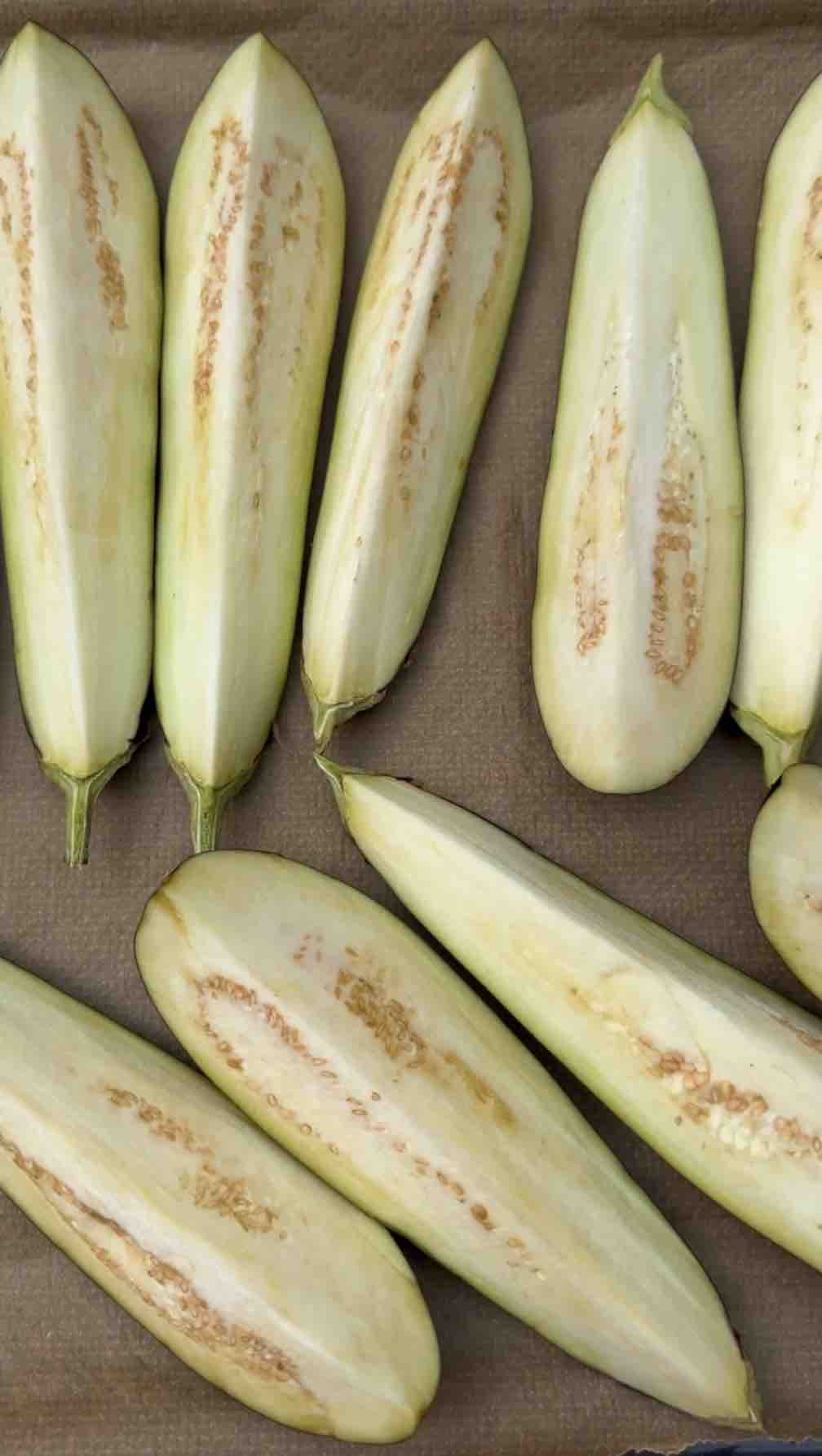 Two eggplants sliced into thick strips aligned on a baking pan. 