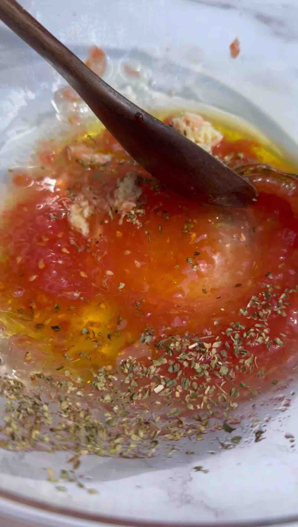 In a bowl, grated tomatoes create a pulp without the skin. Crushed garlic, oregano, lemon juice, olive oil, salt, and pepper are added and mixed together.