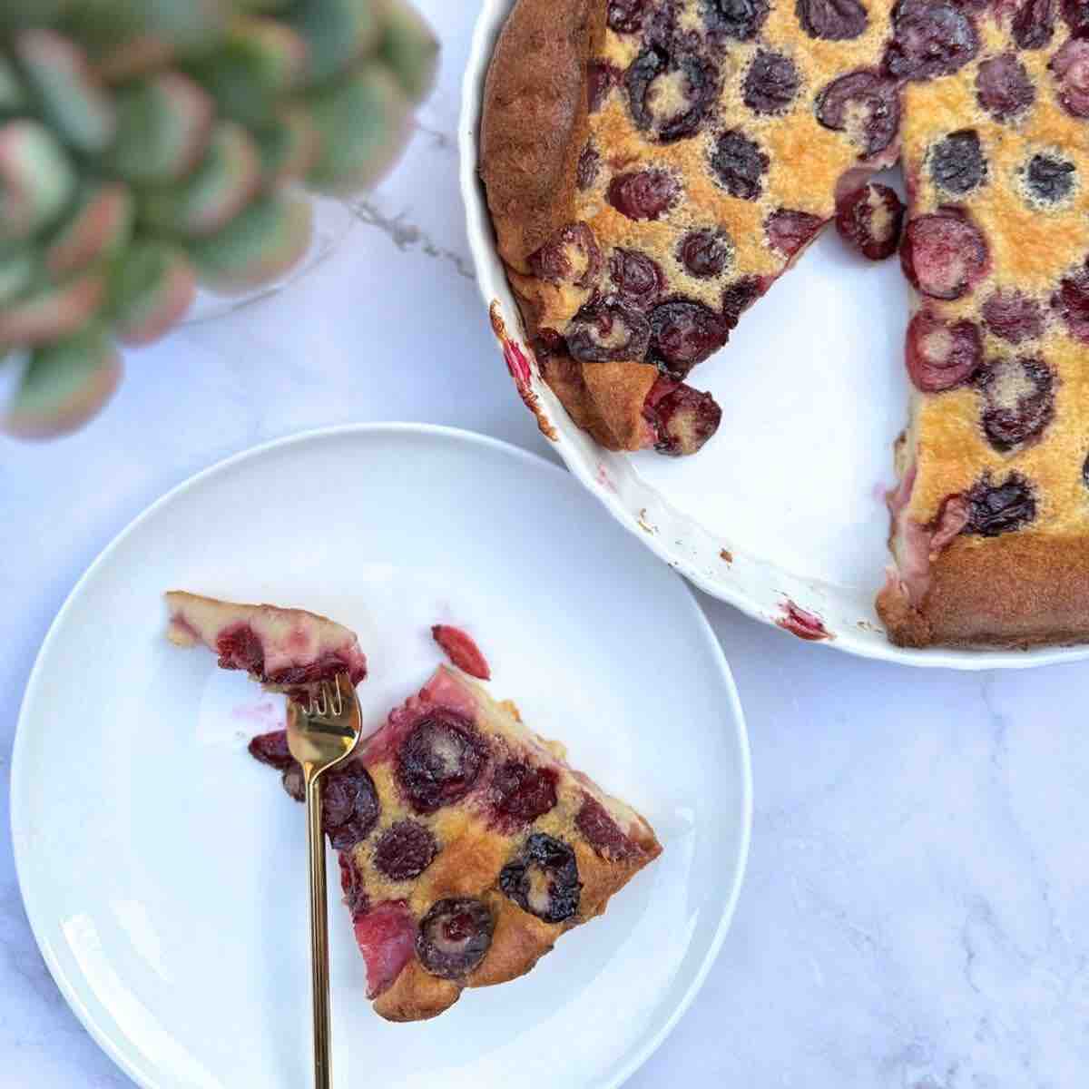 Cherry Clafoutis: A slice on a plate and the rest on the baking ceramic pan