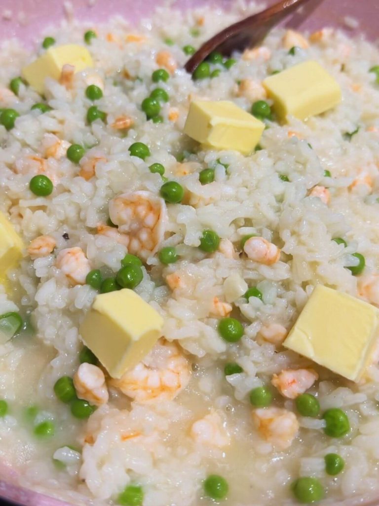 Adding butter cubes to prawn risotto in a pan for creamy goodness