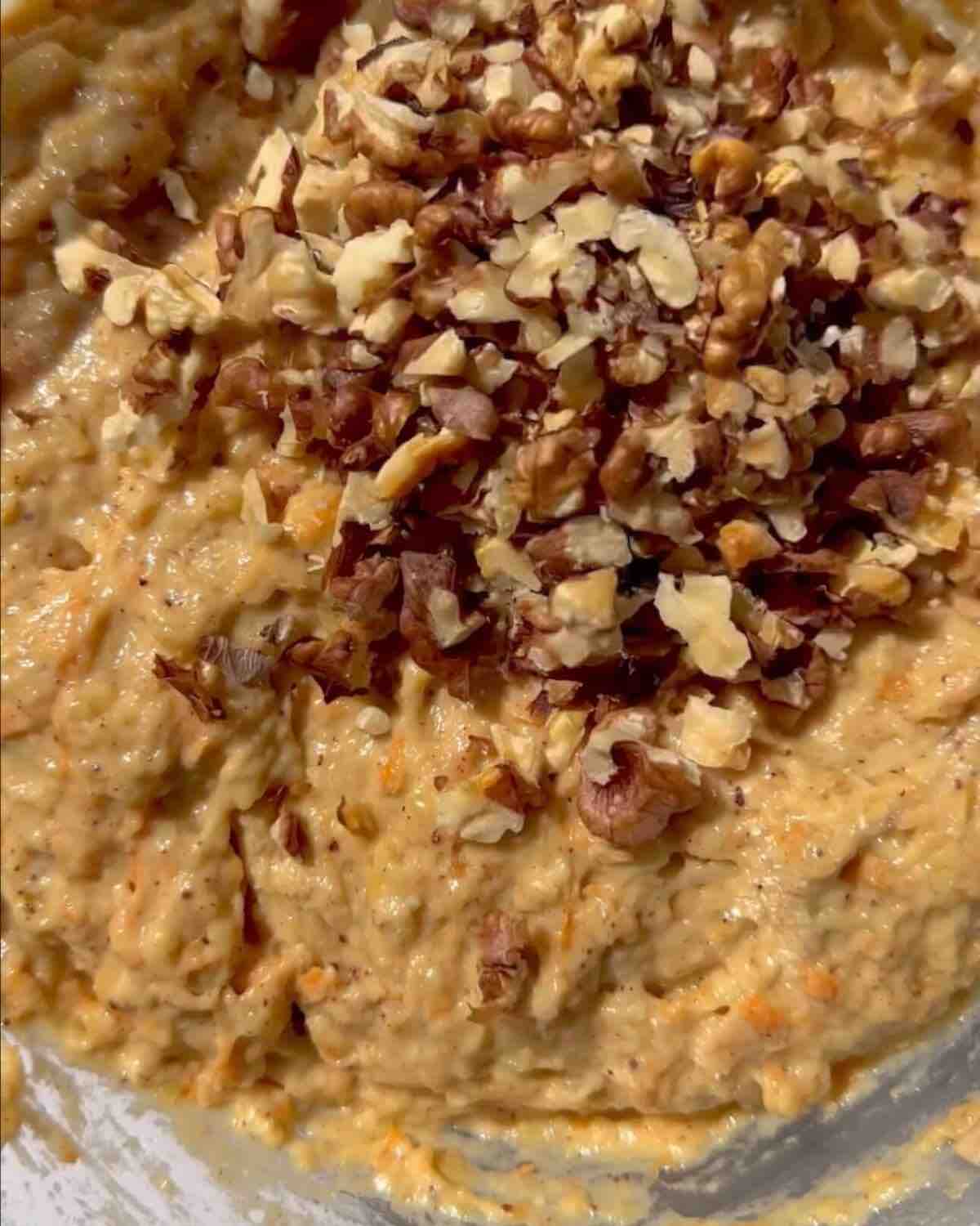 A bowl of smooth batter with chopped walnuts on top, ready to be mixed.
