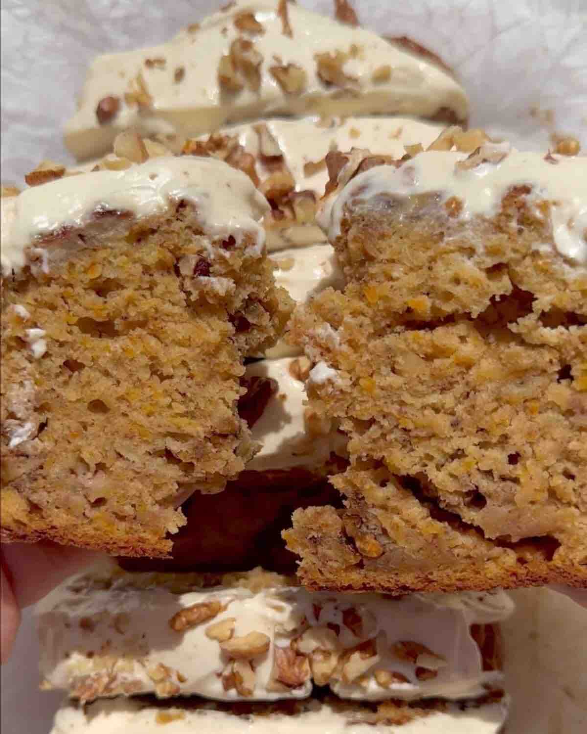 A frosted vegan carrot banana bread topped with walnuts, with a broken slice in front showing its texture.