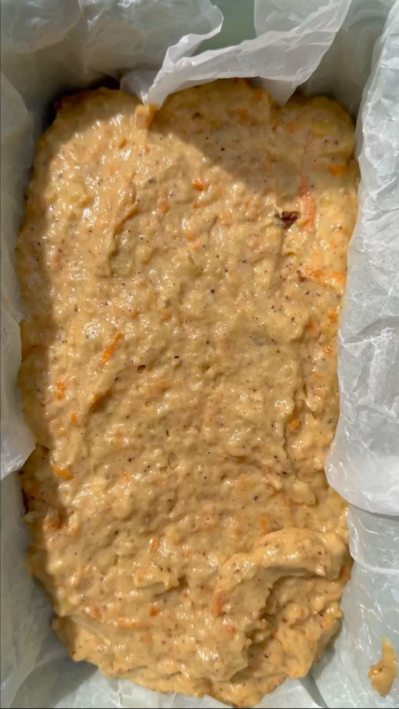 Vegan carrot cake banana bread batter added to a loaf pan lined with parchment paper. 