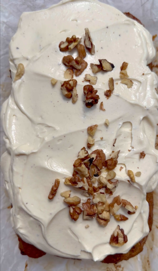Vegan carrot cake banana bread topped with cream cheese frosting and chopped walnuts.