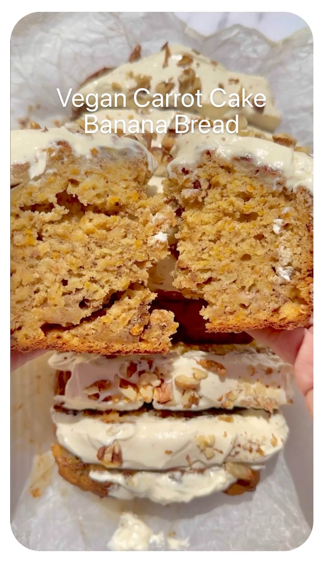 Vegan carrot cake banana bread topped with cream cheese frosting and walnuts, held in hand with a slice torn in half.