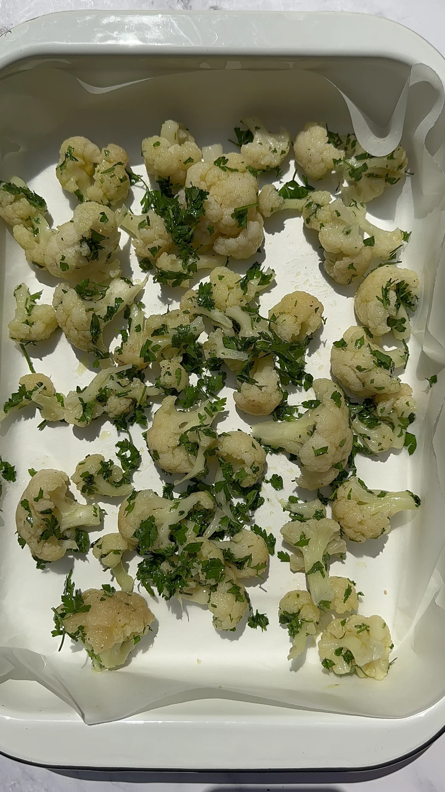 cauliflower florets garnished with chopped parsley and olive oil in a tray before roasting