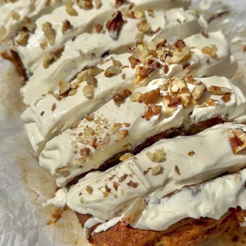 Vegan carrot cake banana bread topped with cream cheese frosting and walnuts.