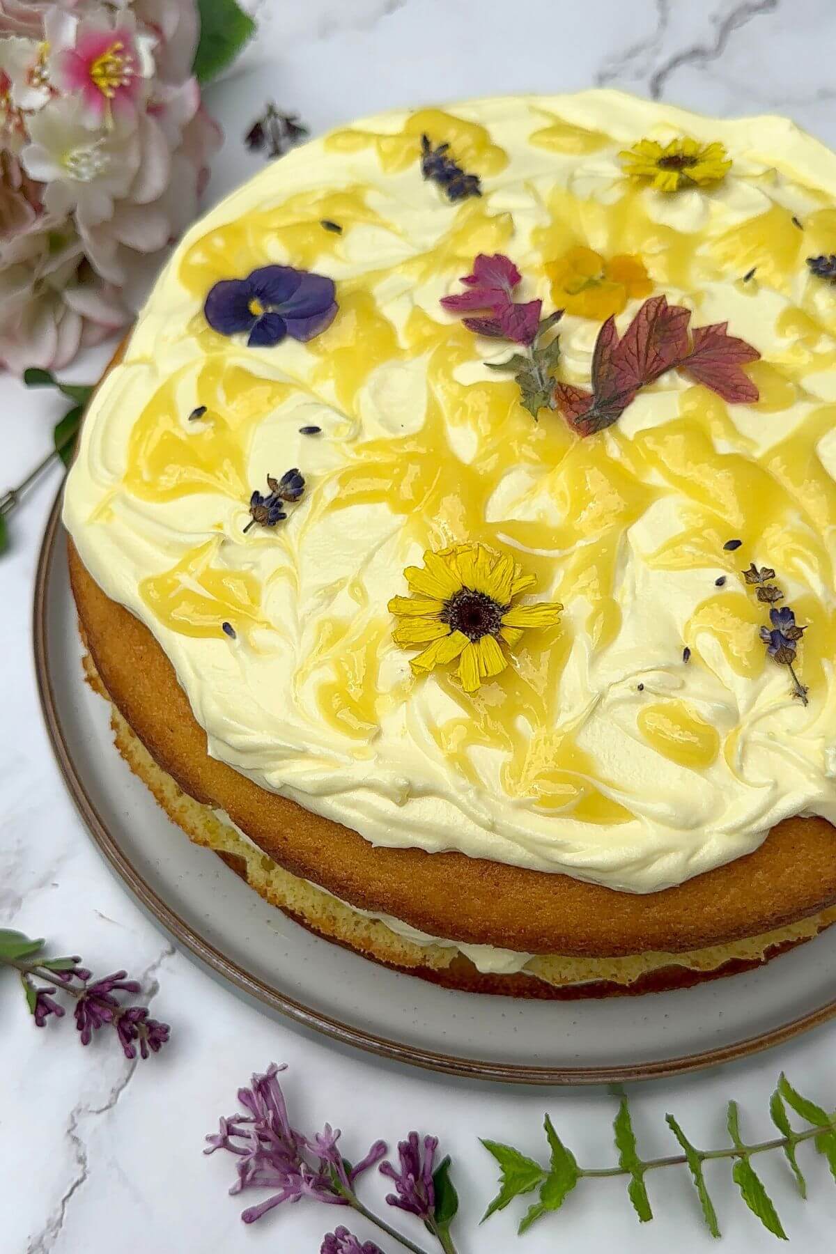Three Layer Lemon Cake decorated with lemon cream cheese frosting, lemon curd swirls and edible flowers.