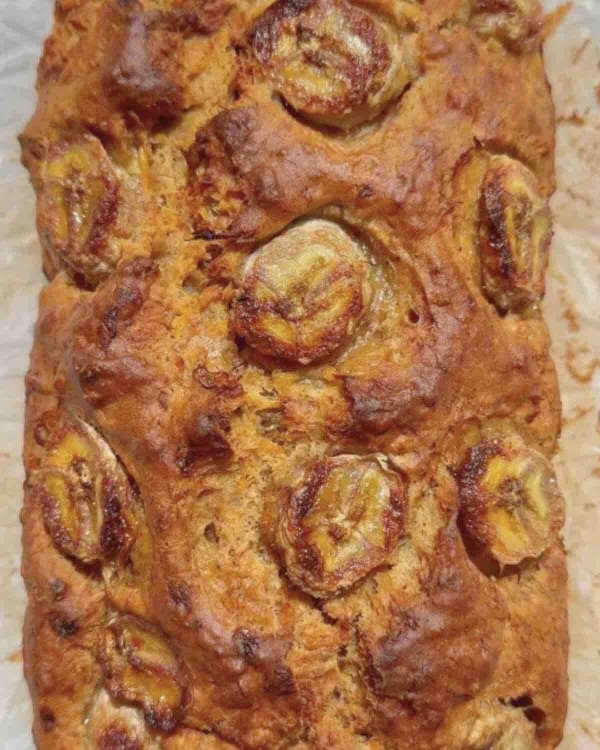 A golden-brown loaf with caramelized banana slices on top, showcasing its rich texture and color.