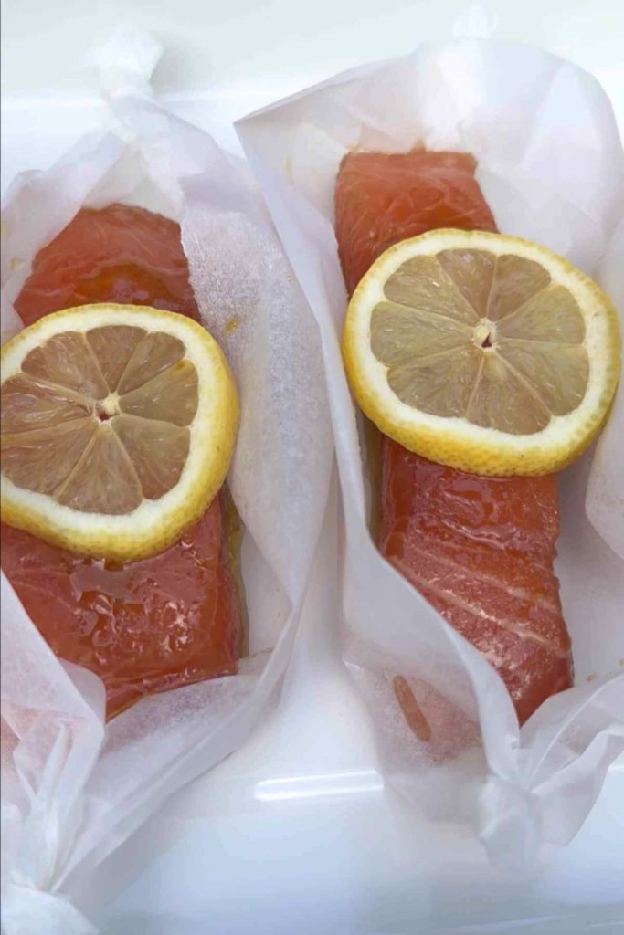 marinated salmon with lemon slices on top placed in parchment paper to be oven baked