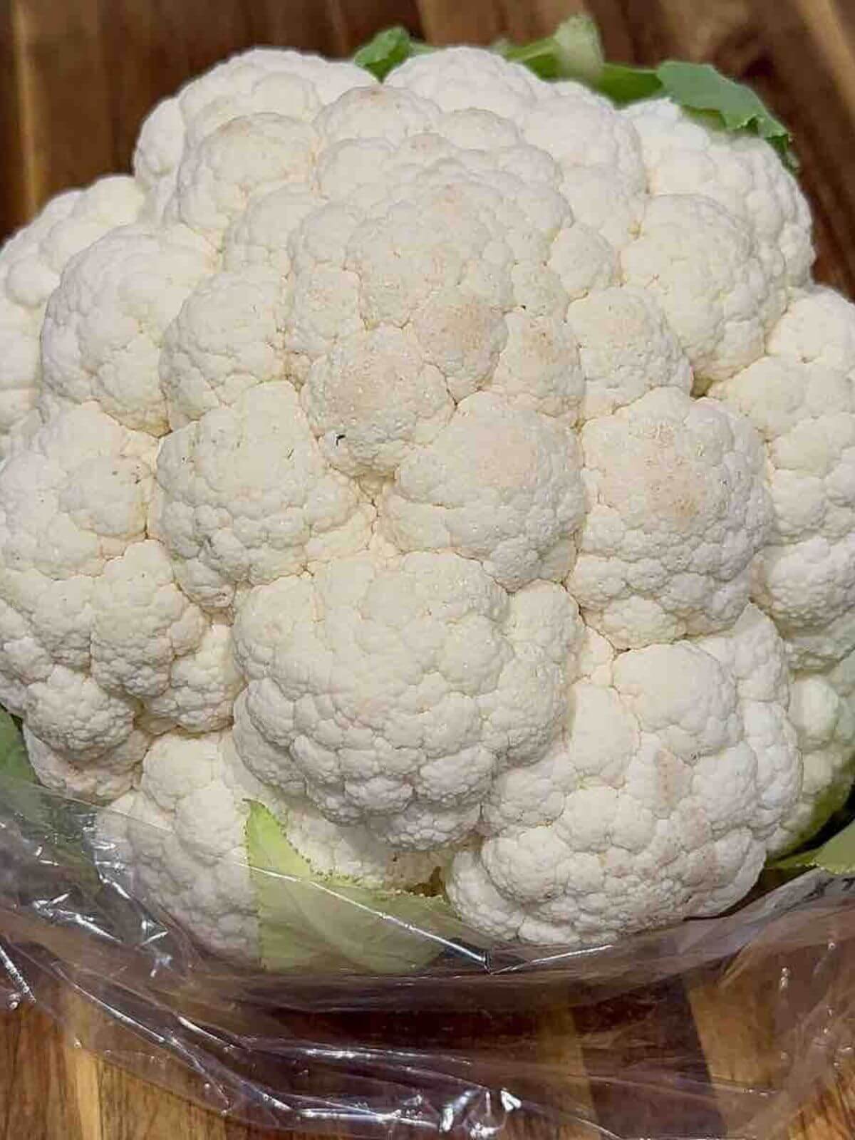 A head of white cauliflower displayed on a rustic wooden board, highlighting its fresh and natural appearance.