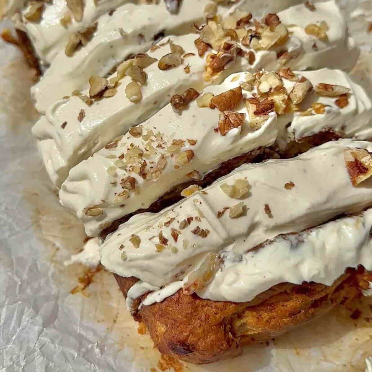 Vegan carrot cake banana bread topped with cream cheese frosting, walnuts.