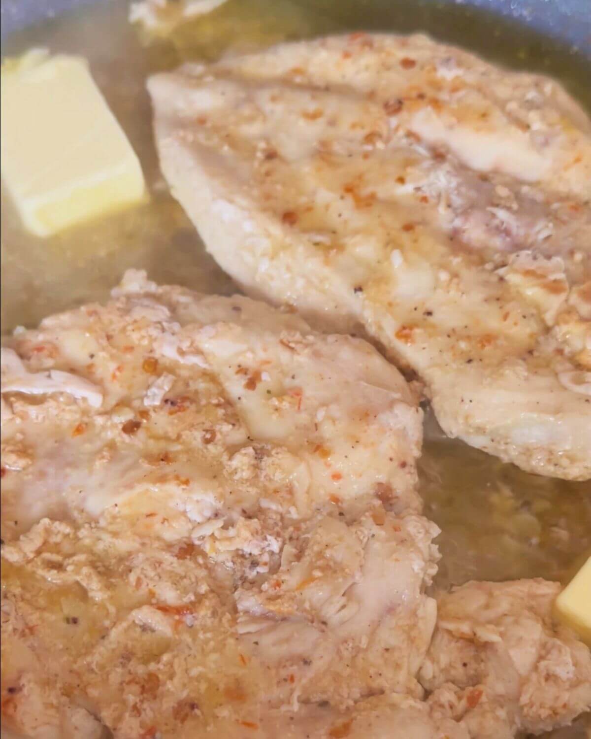 Two pieces of marinated chicken breast, ready to be cooked in a pan with olive oil and butter.