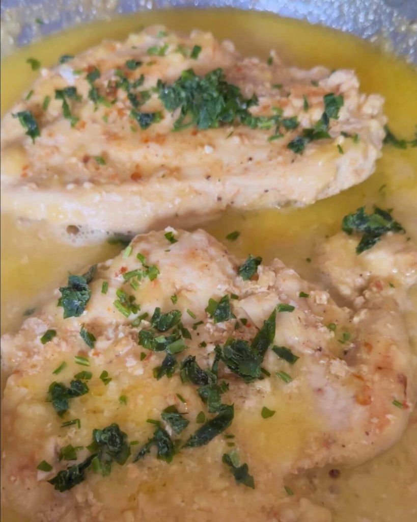 A photo showing two pieces of cooked chicken breast in lemon sauce and garnished with fresh parsley. 