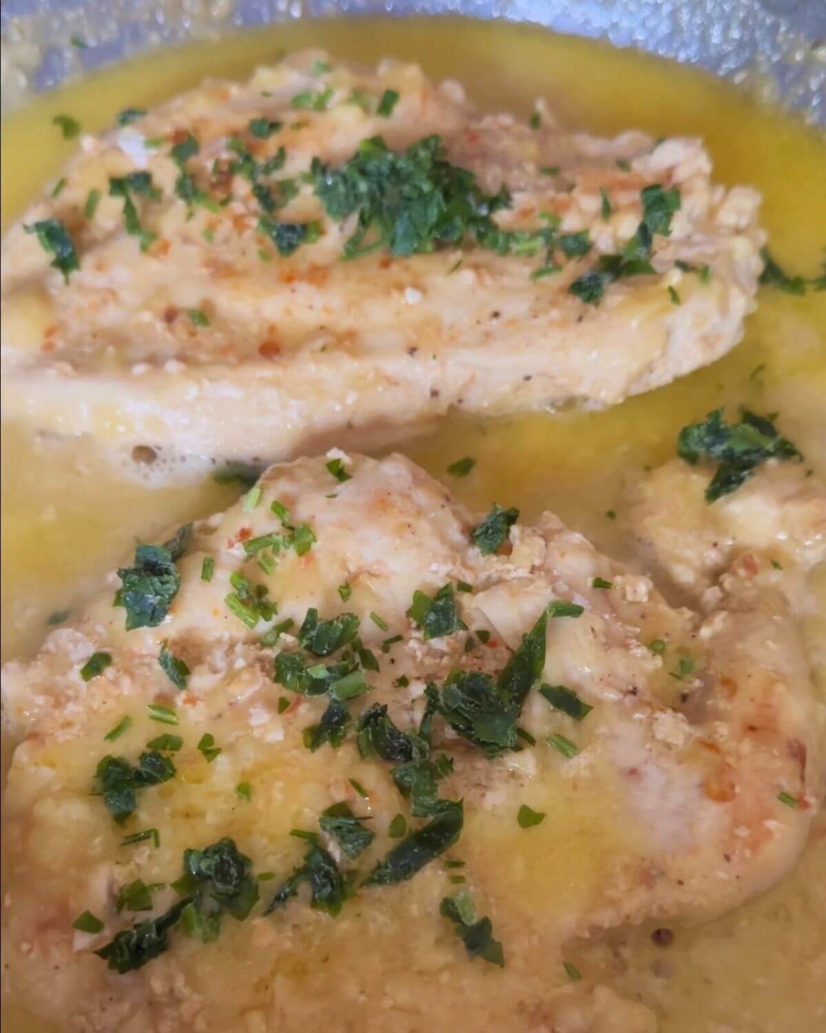 A photo showing two pieces of cooked chicken breast in lemon sauce and garnished with fresh parsley.