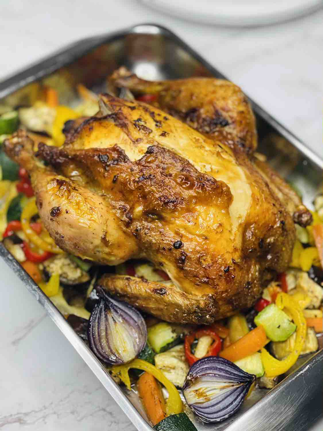 A whole roast chicken with vegetables on a baking tray.