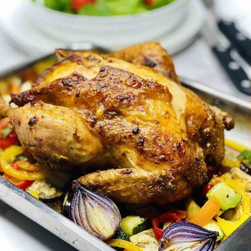 A photo showing a roast chicken in a baking tray with roasted veggies all around.