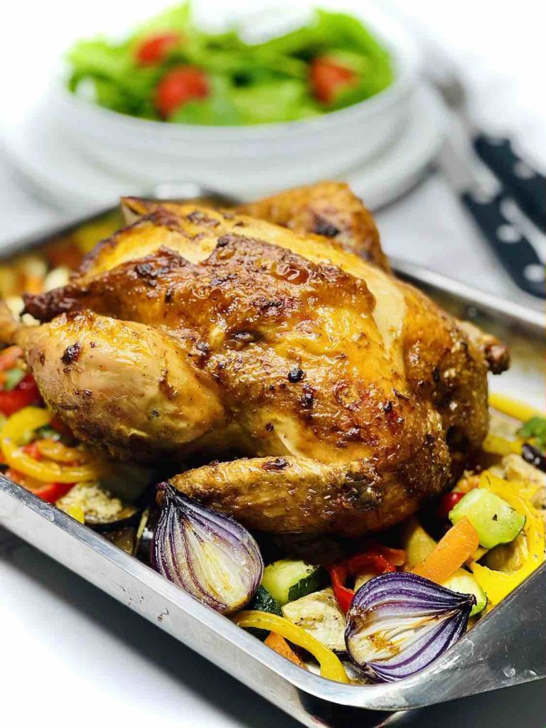 A photo showing a roast chicken in a baking tray with roasted veggies all around.