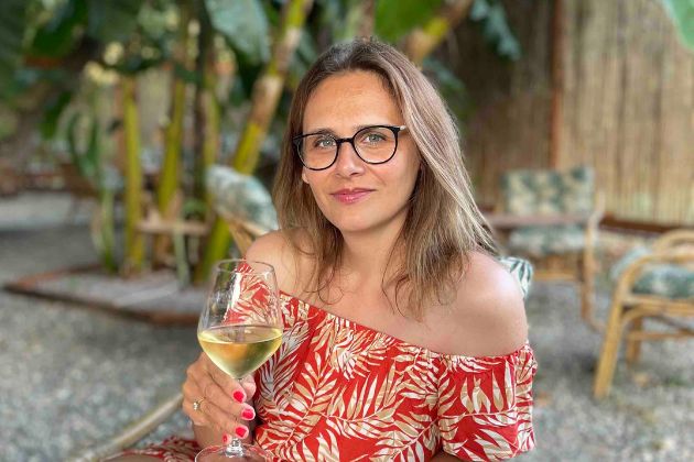 A photo showing the creator of this food blog holding a glass of white wine. 